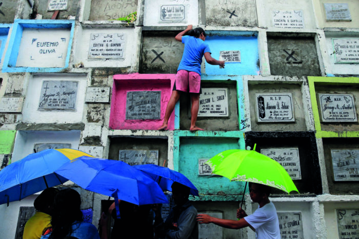 Des personnes portant des bougies et des fleurs dans un cimetière de Manille, aux Philippines.