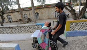 A volunteer carrying a person with a disability in a wheelchair.